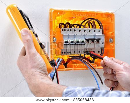 Electrician Technician Working On A Residential Electrical Panel, Measures The Voltage On The Termin
