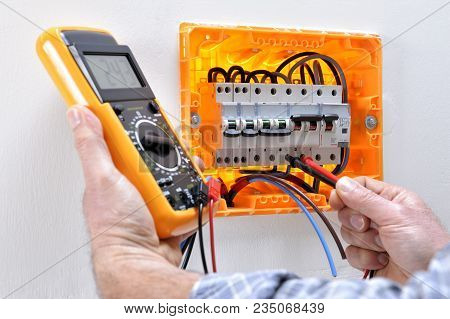 Electrician Technician Working On A Residential Electrical Panel, Measures The Voltage On The Termin