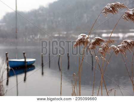 Winter Landscape With Snowy Tufts Of Grass And The Lonely Boat Moored On The Jetty Of The Lake