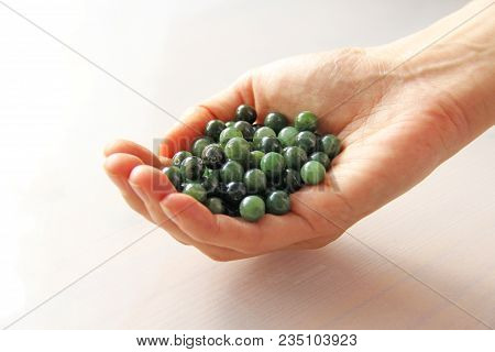 Natural Green Jade Nephrite Mineral Stones Beads. The Green Jade Stone Lies In The Hands. Hands Hold