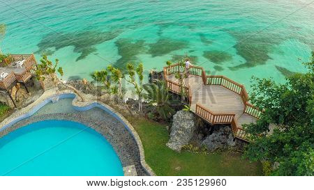 A Beautiful Light Green Coast With Reefs And A Loving Couple On The Balcony Above The Beach. The Bea