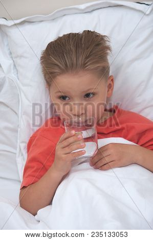 Little Sick Cute Cboy Holding A Pill And A Glass Of Water Lying On The Bed