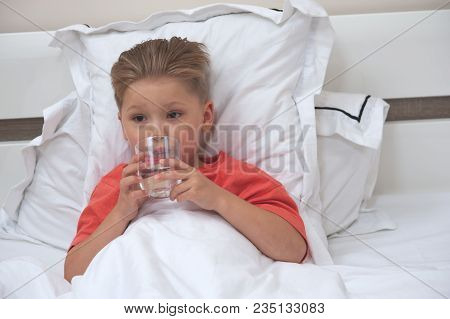 Little Sick Cute Cboy Holding A Pill And A Glass Of Water Lying On The Bed
