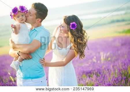 Mom, Dad And Their Little Daughter In A Beautiful Wreath Are Walking In A Lavender Field. Life In Pr