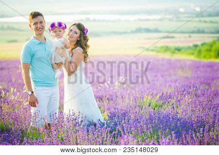 Mom, Dad And Their Little Daughter In A Beautiful Wreath Are Walking In A Lavender Field. Life In Pr