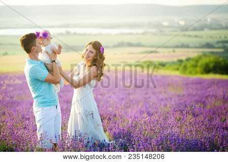 Mom, Dad And Their Little Daughter In A Beautiful Wreath Are Walking In A Lavender Field. Life In Pr