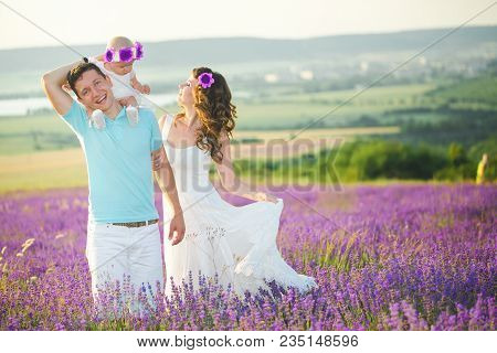 Mom, Dad And Their Little Daughter In A Beautiful Wreath Are Walking In A Lavender Field. Life In Pr