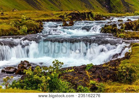 Rumbling cascading waterfall in Iceland. Wide picturesque valley along highway number one around the island. Travel in Iceland. Concept of active and extreme tourism