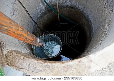 Iron Bucket With Water At The Depth Of A Round Well