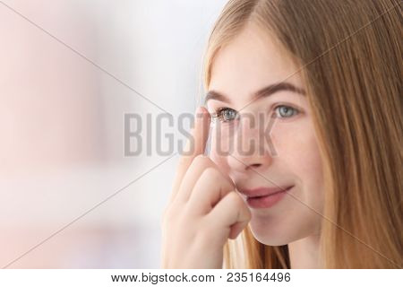 Teenage Girl Putting Contact Lens In Her Eye On Blurred Background