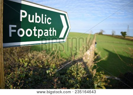 Closeup Of A Public Footpath Sign Taken With A Shallow Depth Of Field, Pointing Across A Green Field