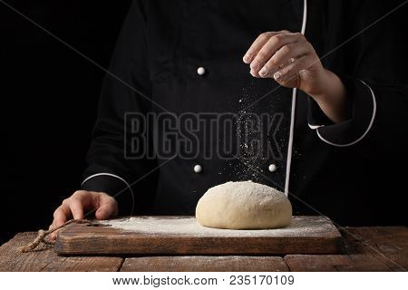 Chef Hands Pouring Flour Powder On Raw Dough Using Sieve On A Black Background, Cooking Process.