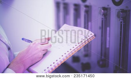 A Young Doctor Woman Is Writing Down Some Medical Chemical Analyses In Front Of A Laboratory Equipme