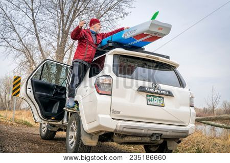 Fort Collins, CO, USA - April 7,2018: A senior male paddler is unloading his racing stand up paddleboard from the roof of Toyota 4runner SUV, a lake shore in early spring scenery.