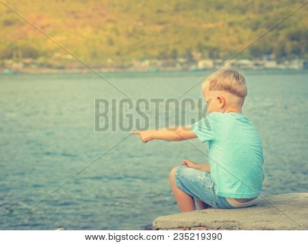 Cute caucasian boy pointing at seaside. Rear view. Leisure time