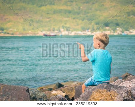 Cute caucasian boy pointing at seaside. Rear view. Leisure time