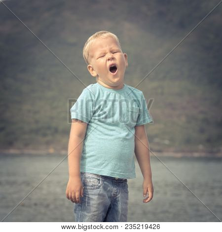 Cute caucasian boy yawns at seaside. Leisure time