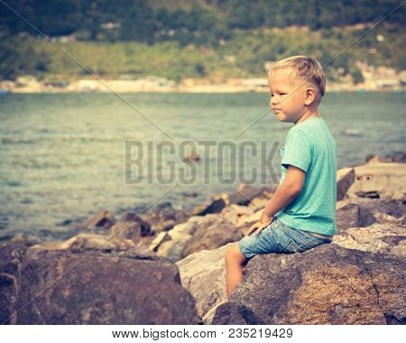Cute caucasian boy sitting at seaside. Leisure time