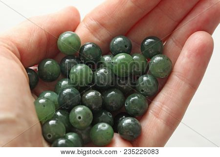 Natural Green Jade Nephrite Mineral Stones Beads. The Green Jade Stone Lies In The Hands. Hands Hold
