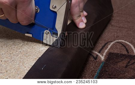 Hands Upholstering The Paricle Board Using Blue Stapler And Brown Leather. Close Up