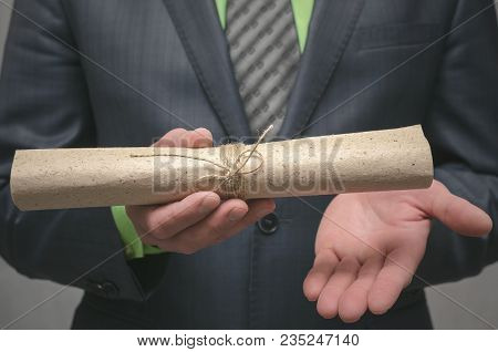 Businessman Holds In Hand A Rolled Up Document Scroll. Signing Of An Agreement. Conclusion Of A Busi