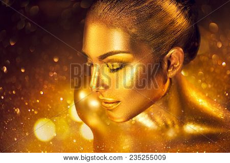 Fashion art Golden skin Woman face portrait closeup. Gold jewellery, jewelry, accessories. Beauty gold eyes, Lips, Skin and hair. Model girl with holiday golden Glamour shiny professional makeup