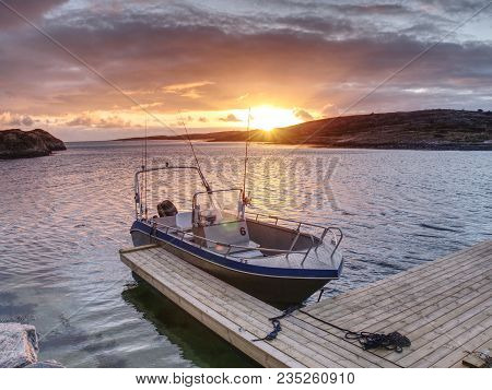 Fishing Boat Anchored In Silent Bay, Evening Sun At Horizon.  Small Ship With Fishing Rods At Wooden