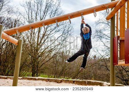 Happy Boy Hanging On Ladder In The Playground Outdoors