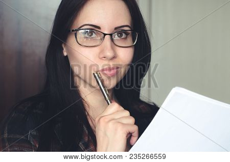 Young Caucasian Girl With Glasses Holds A Pen And A Document And Thinks. Concept Of Passing Exams, T