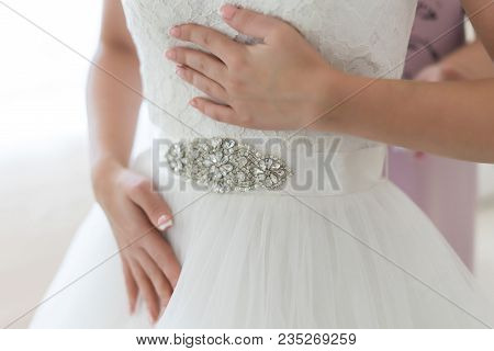 Gentle Bride Holds Her White Lace Wedding Dress With Crystal Ornament On The Belt, While Her Mother 