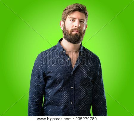 Young hipster man with big beard making funny face fooling over green background