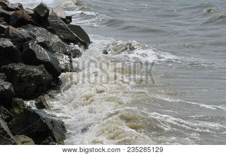 Waves Break Against Dark Stones On The Seashore, Sun Glare On The Rocks