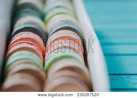Multicolored Macaroons Lie In A Box On A Turquoise Background Cloose-up.
