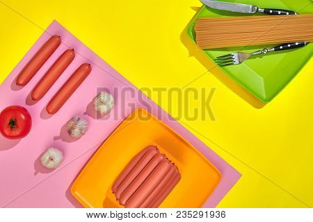 A Lot Of Raw Sausages On Plate. On Yellow Background With Pasta And Vegetables, Top View. Still Life