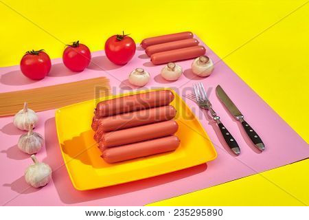 A Lot Of Raw Sausages On Plate. On Pink And Yellow Background With Pasta And Vegetables, Top View. S