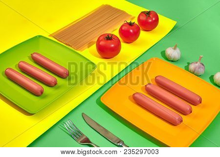 A Lot Of Raw Sausages On Plate. On Green And Yellow Background With Pasta And Vegetables, Top View. 