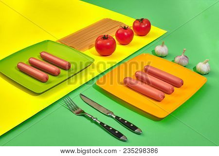 A Lot Of Raw Sausages On Plate. On Green And Yellow Background With Pasta And Vegetables, Top View. 