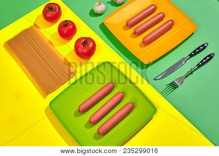 A Lot Of Raw Sausages On Plate. On Green And Yellow Background With Pasta And Vegetables, Top View. 
