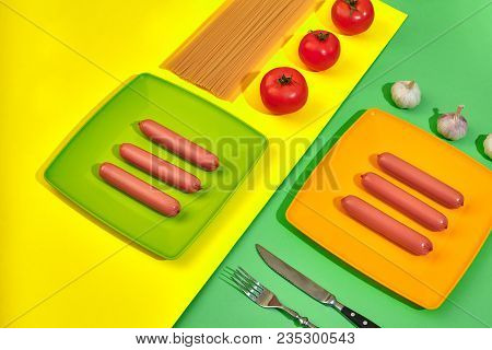 A Lot Of Raw Sausages On Plate. On Green And Yellow Background With Pasta And Vegetables, Top View. 