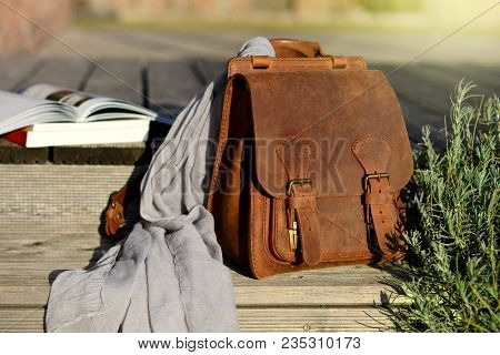 vintage style natural leather brown backpack and books on gray rustic wooden stairs