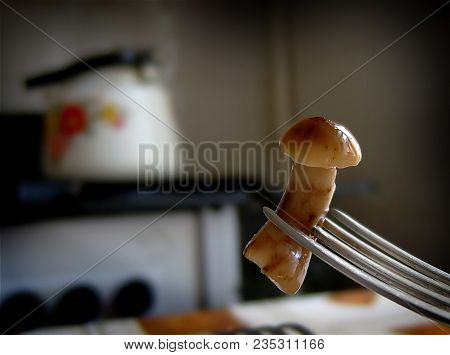 Marinated Mushroom On A Fork. Close-up. The Kettle On The Stove Is On The Background