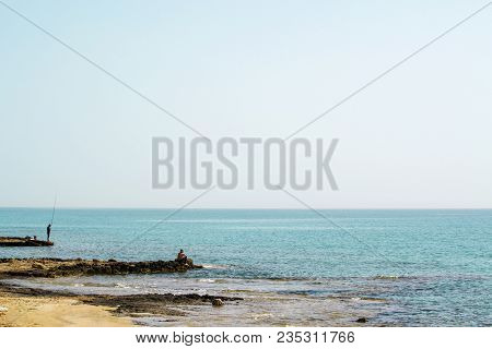 Two Fishermans Staying On The Rocky Shore With Rods