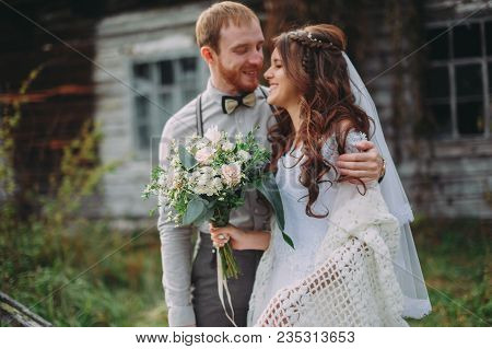 Stylish Bride And Groom On The Background Of Wooden Houses .rustic Wedding Couple