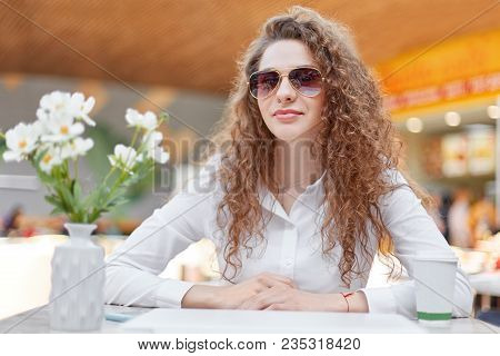 Portrait Of Beautiful Woman With Curly Hair, Healthy Skin, Wears Trendy Shades, Looks Confidently At