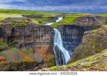 Foggy July day in Iceland. The concept of extreme and phototourism. High waterfall Hayfoss in a picturesque and dangerous tundra canyon 