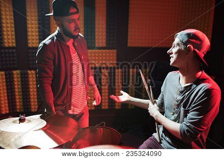 Portrait Of Young Drummer Talking To Frontman In Dim Recording Studio Discussing New Song