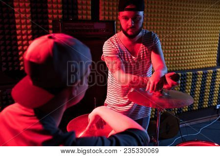 Portrait Of Frontman Talking To Drummer While Writing Music  In Recording Studio Lit By Red Lights W