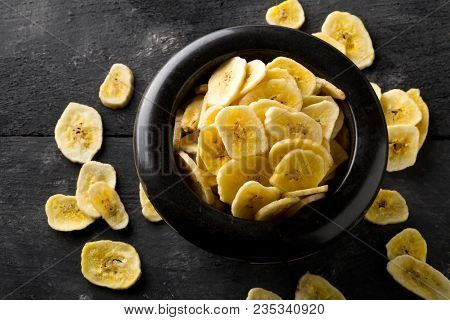 Heap Of Dried Banana Chips Snack In Black Bowl On Dark Rustic Table
