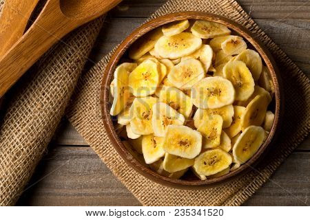 Heap Of Dried Banana Chips Snack In Wooden Bowl On Burlap On Dark Wooden Table Top View