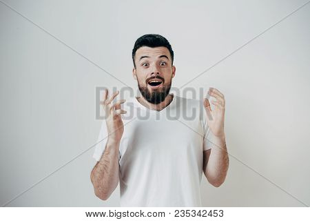 Handsome Guy Is Standing Near White Wall And Keeping His Hands Up. He Is Very Excited And Happy. Iso